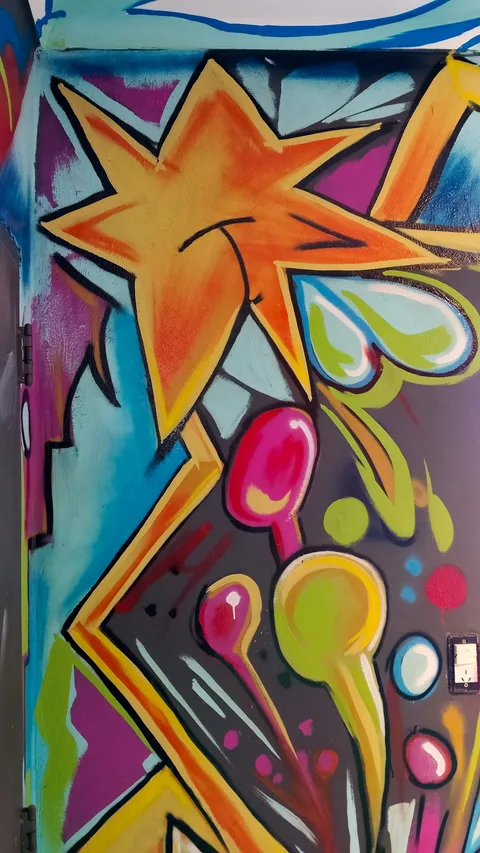 Columna pintada con una gran estrella naranja sonriente, globos magenta y verde lima y rayos amarillos, sobre fondo turquesa y violeta.