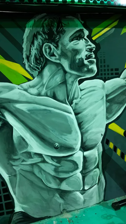 Detalle del rostro y el torso del mural: pintura realista en grises y verde menta sobre una pared gris con formas geométricas amarillas y verdes.