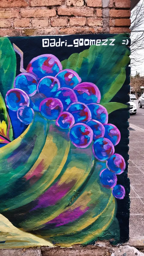 Racimo de uvas azules y violetas dentro de un cuerno verde y dorado, pintado con pinceladas sueltas sobre fondo negro, con la firma @adri_goomezz arriba.